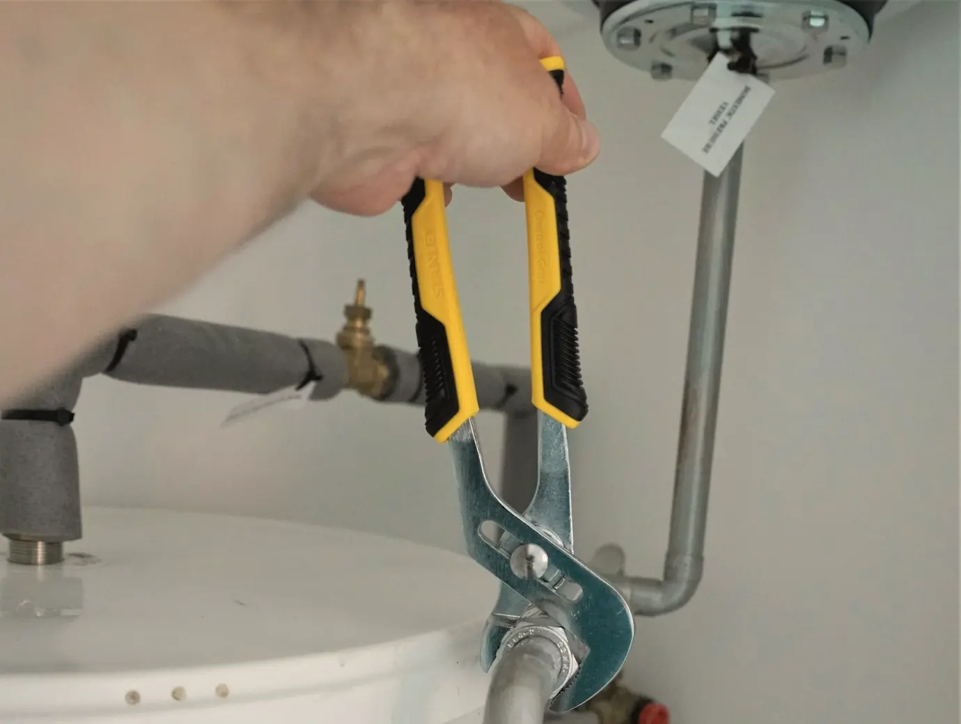 Pliers tightening a supply fitting on top of a tank water heater